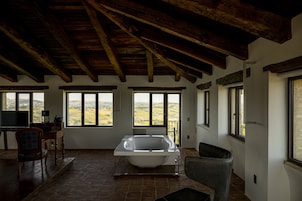 Una habitación amplia con una bañera grande, vigas de madera y ventanas que dan al campo.