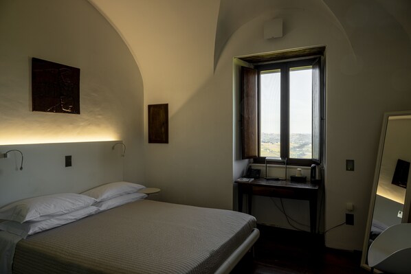 Un dormitorio con cama, escritorio, ventana y vistas a la ciudad.