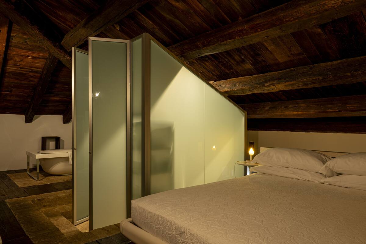 A bedroom with a bed, a nightstand, a bedside table, and a glass partition.