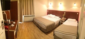 A hotel room with two beds, a TV, a bedside table with a lamp, and a window with curtains. - Ayvazali Hotel (Bergama)