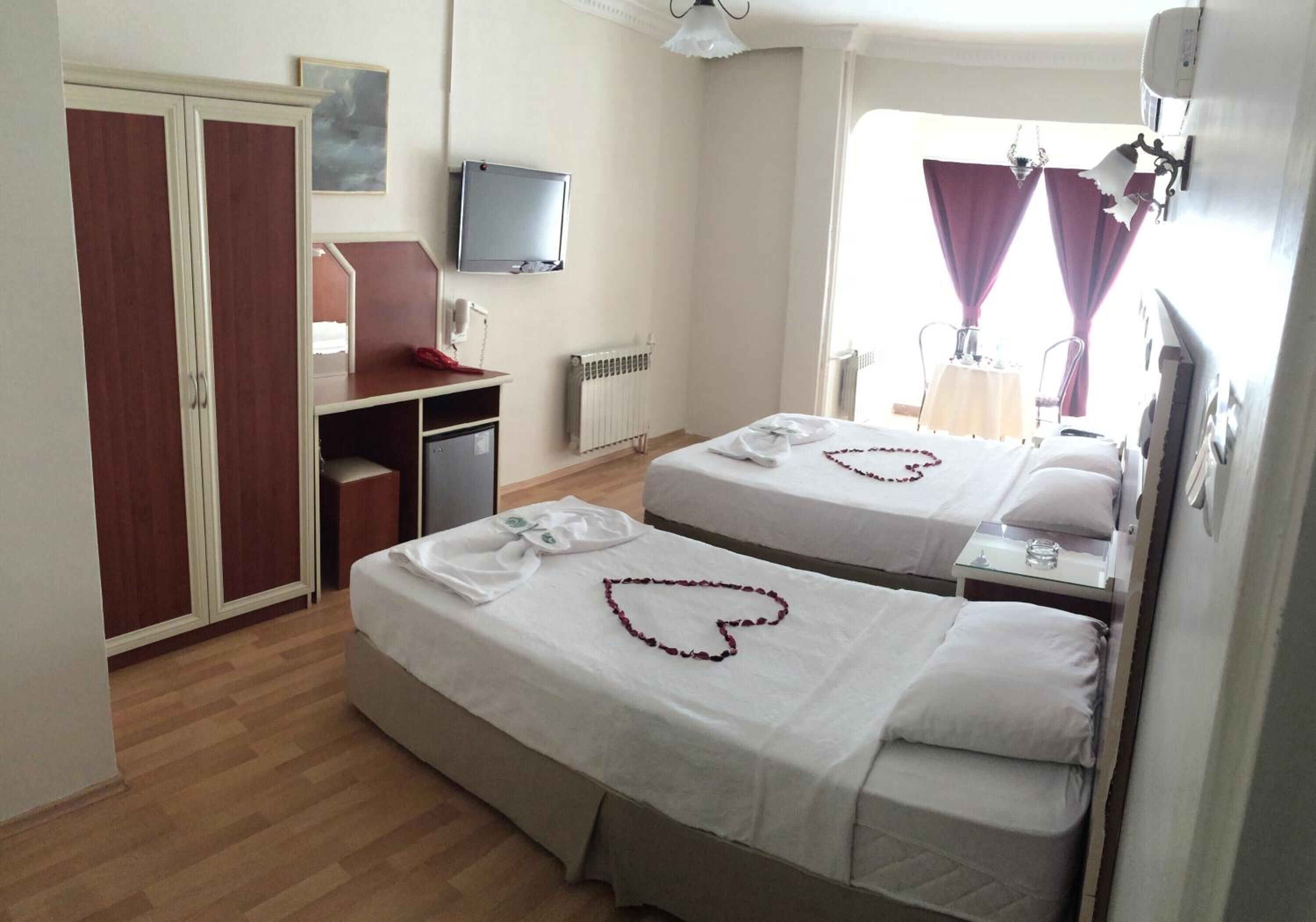 Habitación de hotel con dos camas, un escritorio, un armario, televisión y ventana con cortinas.