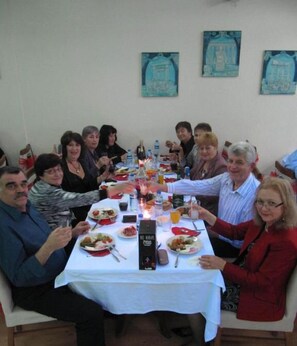 A group of people seated around a table with food and drinks, in a room with plain walls and a simple tablecloth. - Ayvazali Hotel (Bergama)