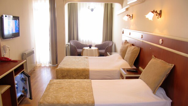 A hotel room with two beds, a TV, a desk with a phone, and a small table with a chair. - Ayvazali Hotel (Bergama)
