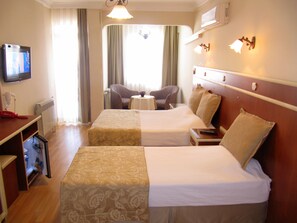 Ein Hotelzimmer mit zwei Betten, einem Fernseher, einem Schreibtisch mit Telefon und einem kleinen Tisch mit Stuhl.