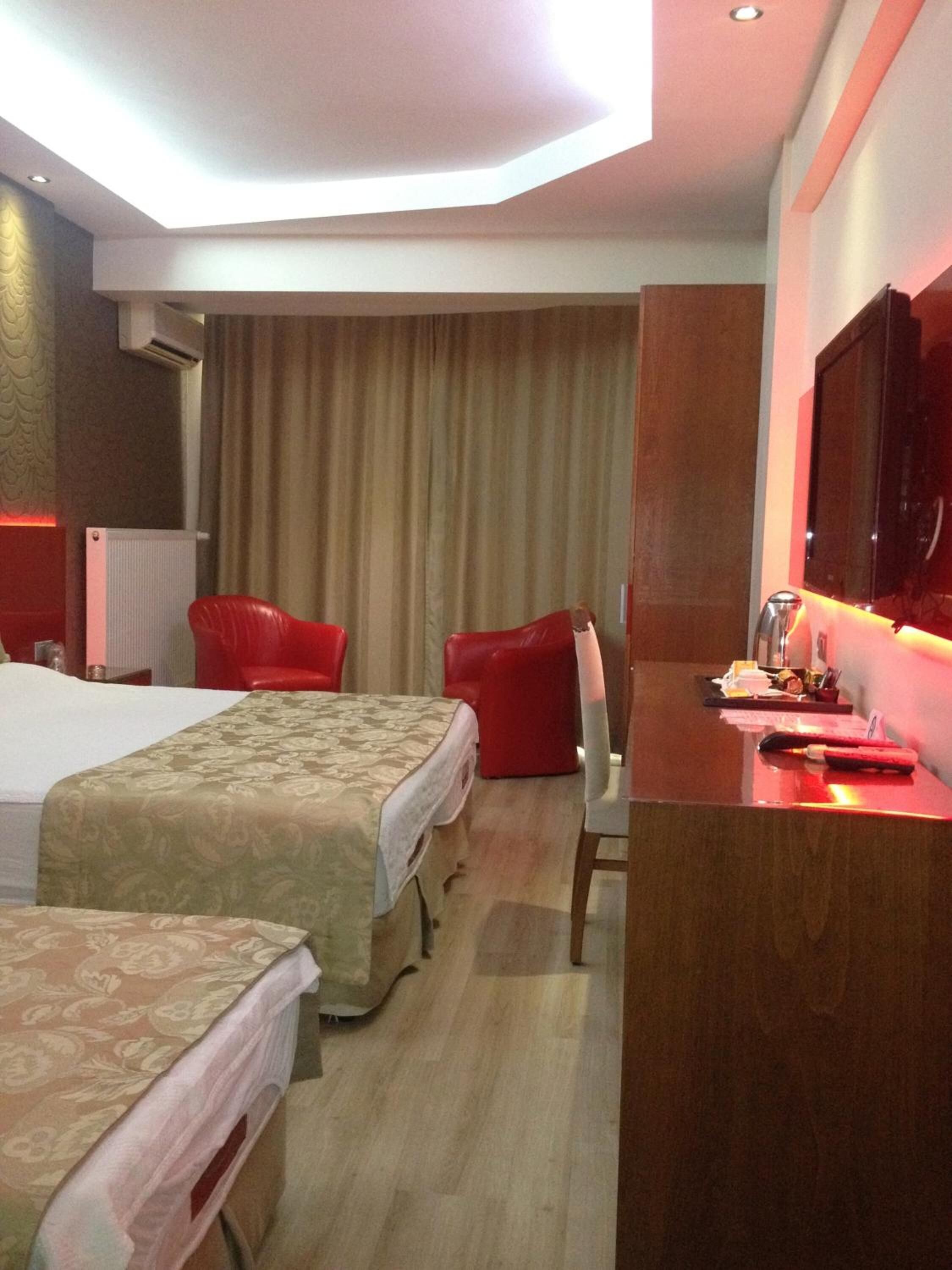 Quarto de hotel com duas camas, uma mesa de trabalho e uma televisão de tela plana, além de uma cadeira vermelha.