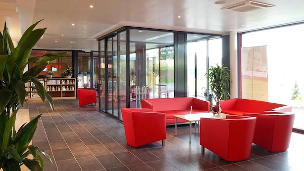 A modern lobby with red seating, a tiled floor, and large windows allowing natural light. - ibis Bulle La Gruyere (Bulle)