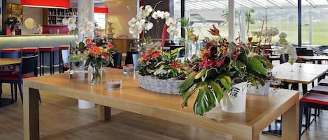 A restaurant with wooden tables, floral centerpieces, and a large window offering a view of the outdoors.