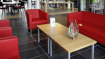 A modern indoor seating area with red chairs and a wooden table, featuring a decorative plant arrangement.