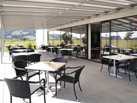 Un caffè all'aperto con tavoli e sedie, ampie vetrate e vista sulla campagna.. ibis Bulle La Gruyere
