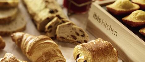 A variety of pastries including croissants and bread, arranged on a table with a label reading "Ibis Kitchen".