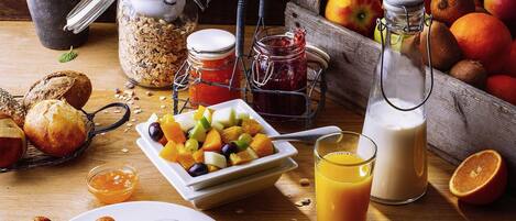 Un desayuno con pan, croissants, queso, fruta y bebidas.