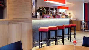 A modern kitchen with wooden cabinets, a bar area with red stools, and a dining table with a martini glass. - ibis Bulle La Gruyere (Bulle)