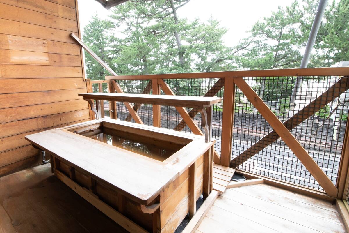 A wooden deck with a wooden table and bench, surrounded by a metal railing and overlooking a wooded area.