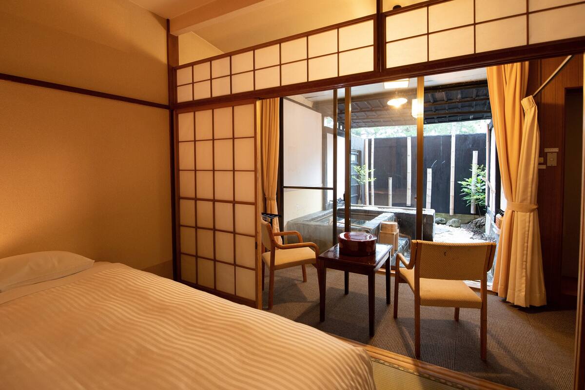 A traditional Japanese-style room with tatami flooring, a low table with a cushion, and a sliding shoji screen.