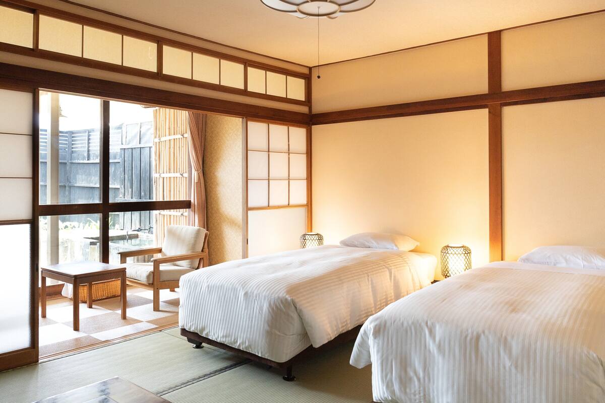 A traditional Japanese-style room with tatami flooring, two beds, a sliding door to a balcony, and a ceiling fan.