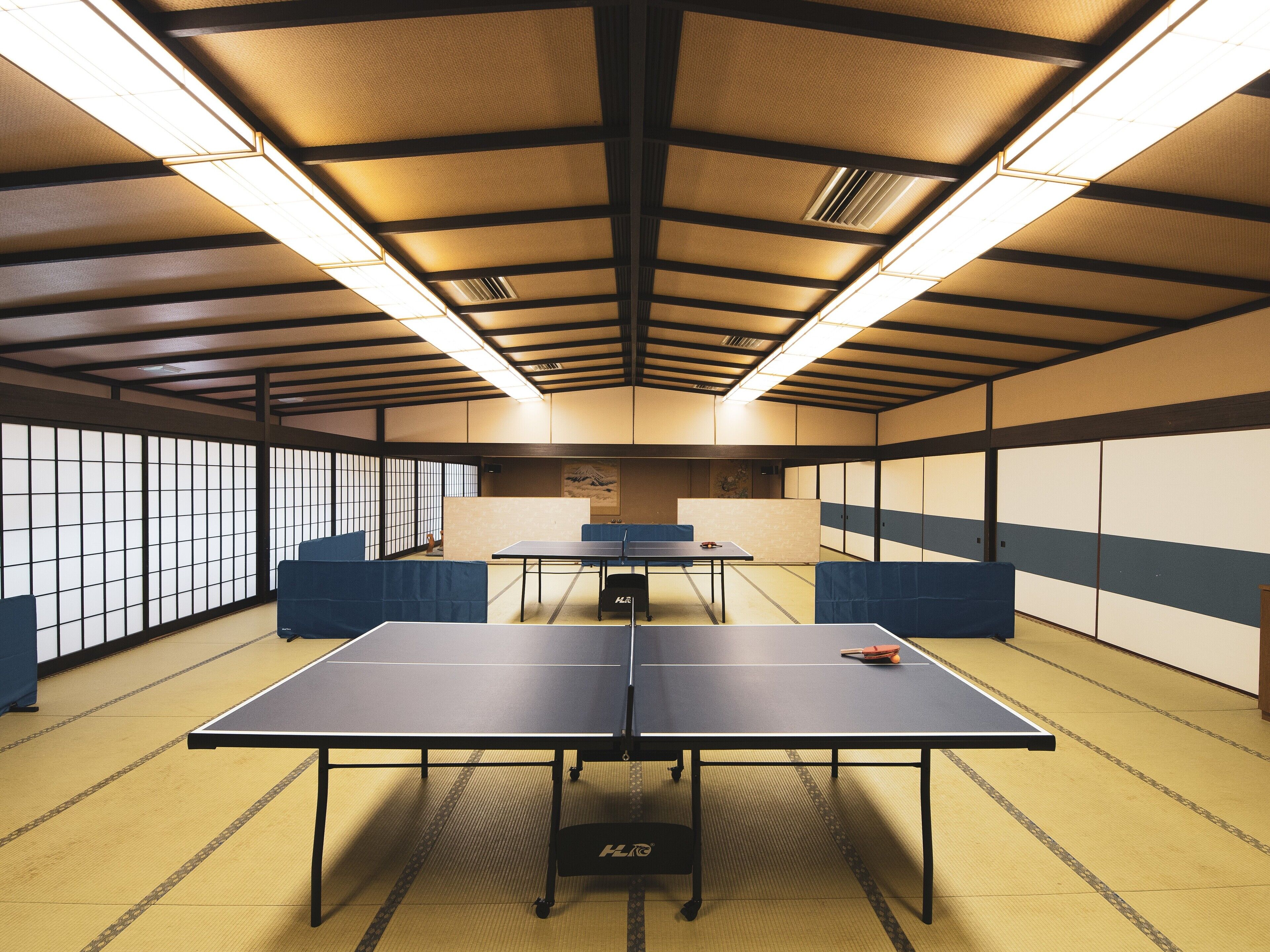 Una habitació amb paviment de tatami, dues taules de ping-pong i portes corredisses tradicionals.