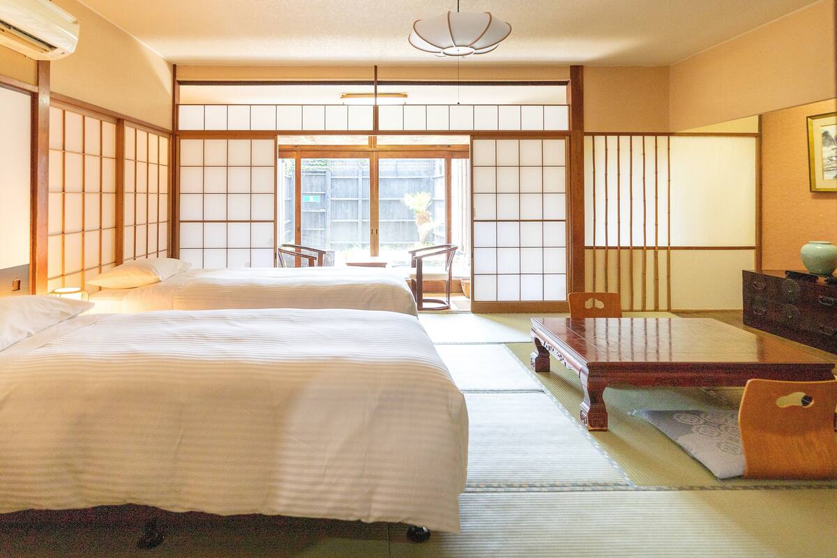 A traditional Japanese-style room with tatami flooring, two beds, a dining table, and sliding doors.