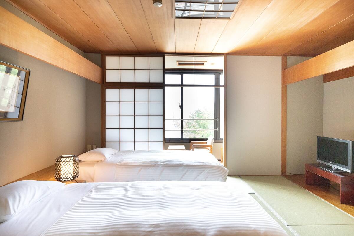 A hotel room with two beds, a television, and a large window.
