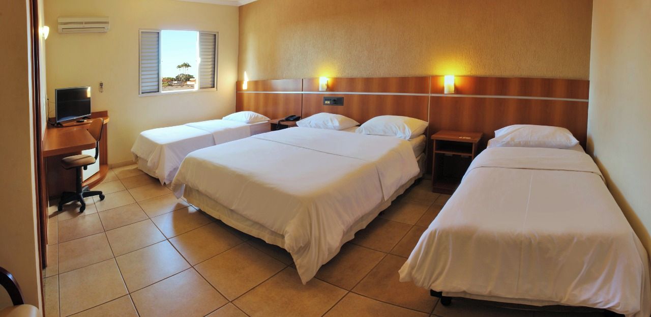 Habitación de hotel con dos camas individuales, un escritorio con computadora y televisión.