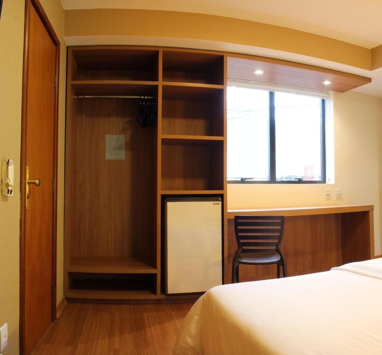 Una habitación pequeña con cama, escritorio, silla, armario y un refrigerador pequeño.