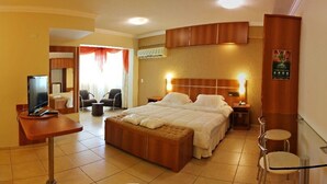 A hotel room with a large bed, a desk with a computer, a TV, and a seating area with chairs. - Bernal Hotel (Ituiutaba)