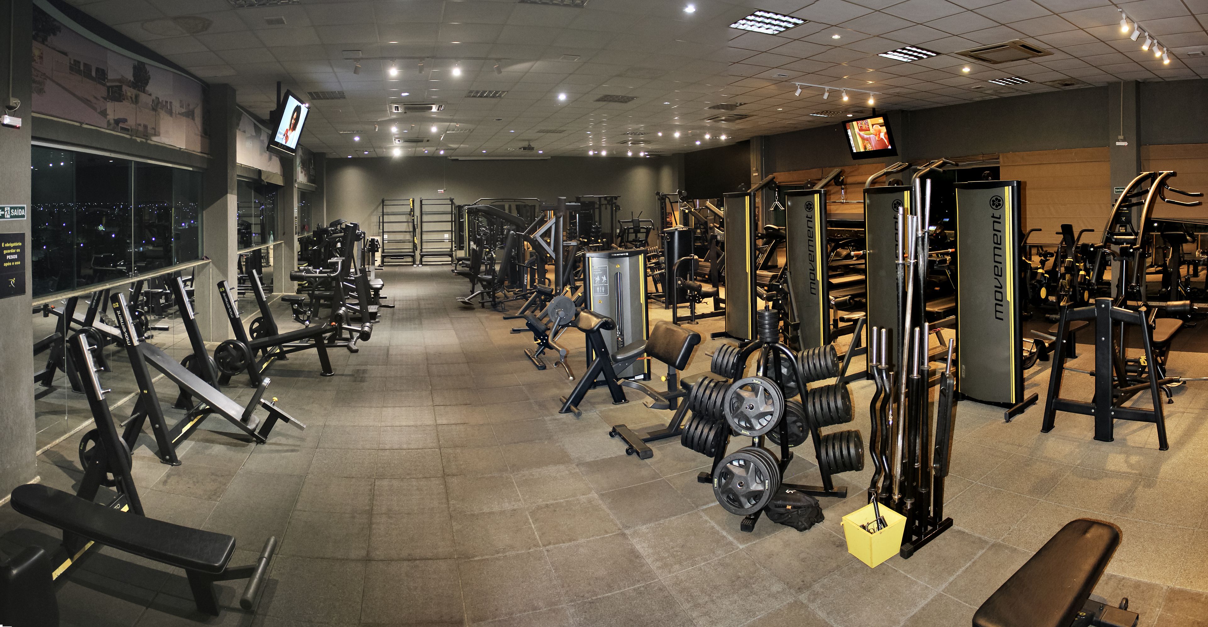 Un gimnasio con varios equipos de ejercicio, incluyendo bancos, máquinas de pesas y pesas sueltas.