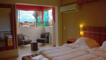 A hotel room with a large bed, two armchairs, a small table, and a window with curtains.