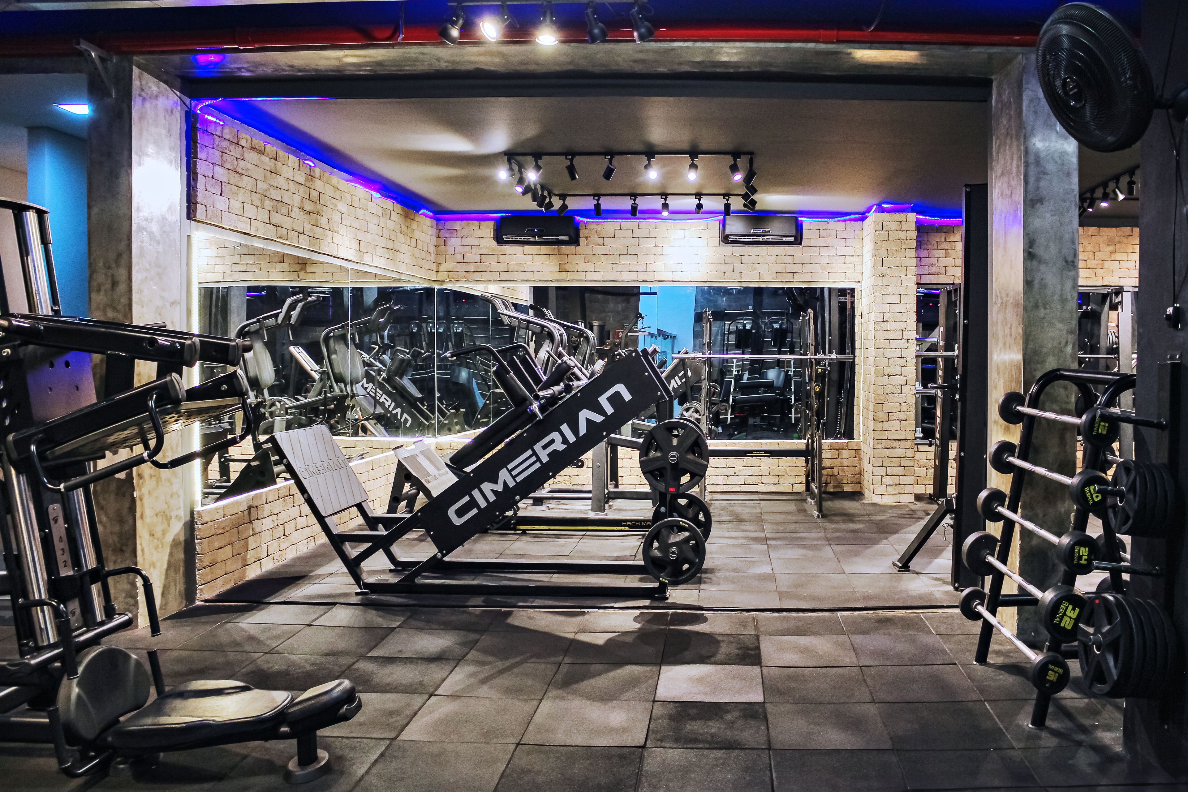 A gym with exercise equipment, a brick wall, and a ceiling fan.