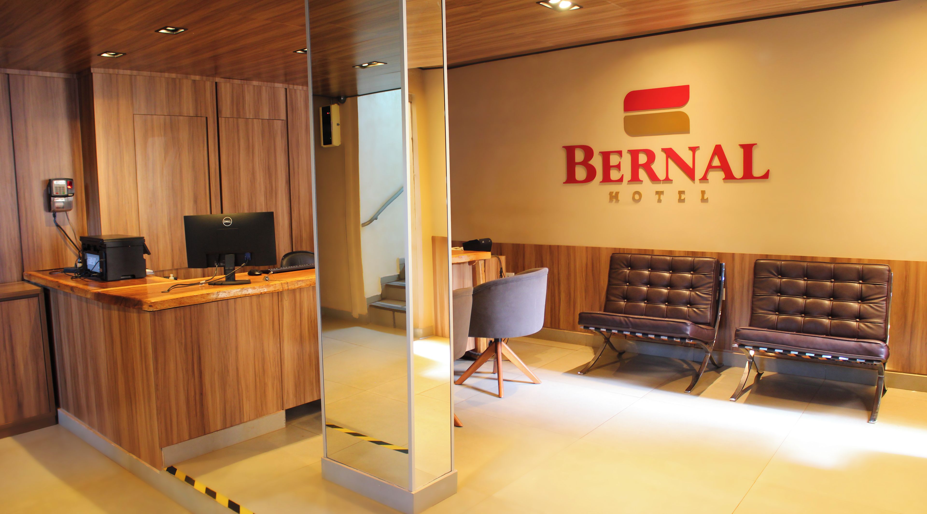 Un mostrador de recepción con una computadora y un teléfono, un letrero que dice Bernal Hotel y dos sillones de cuero.