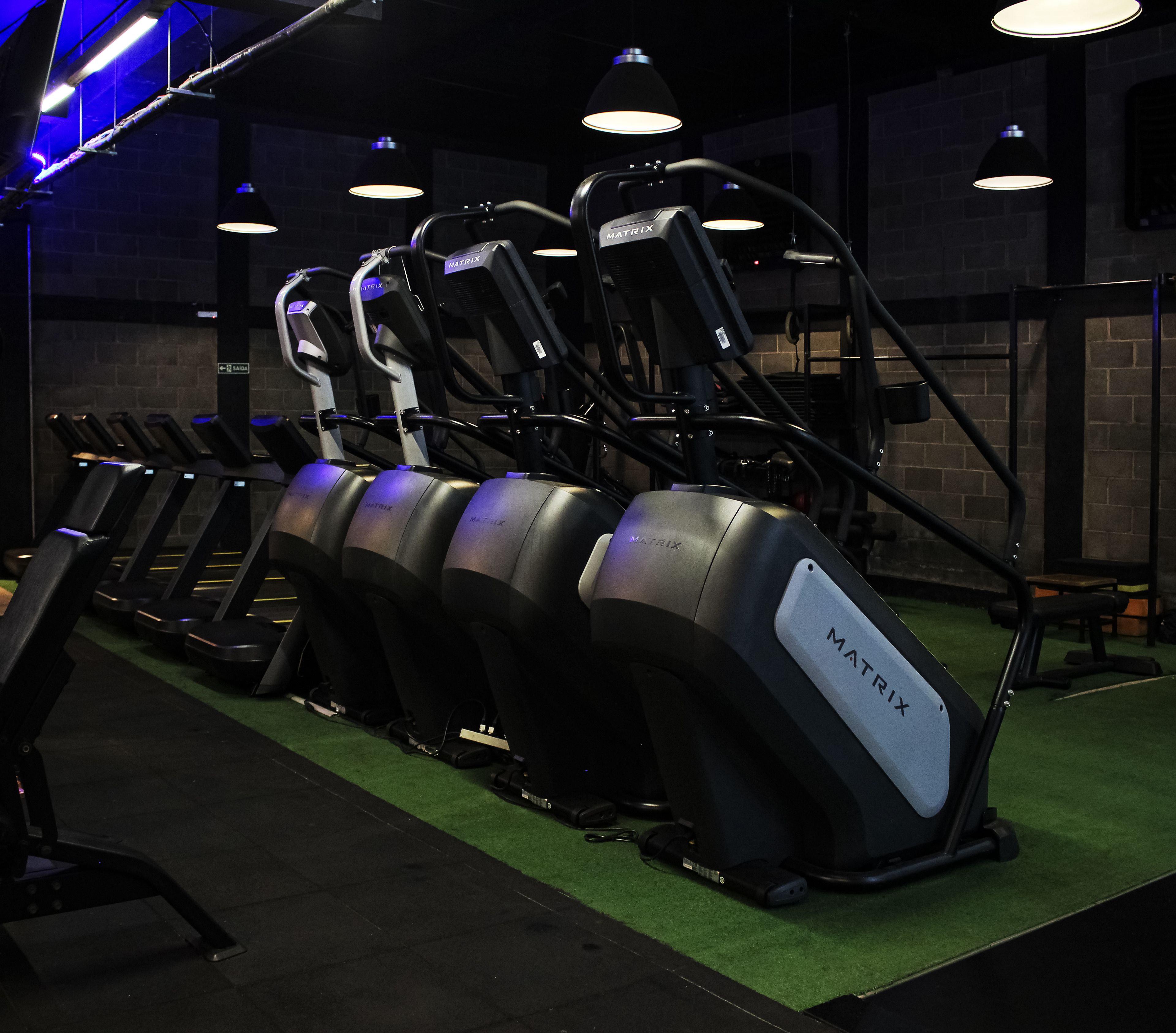 Un gimnasio con cintas de correr, bicicletas estáticas y piso verde.