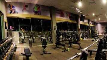 Un gimnasio con diversos equipos de ejercicio, espejos y una pared con anuncios.