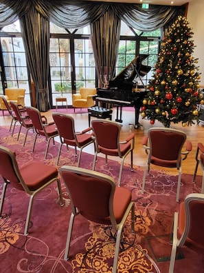 Ein Zimmer mit einem Flügel, einem Weihnachtsbaum und roten Sesseln, die zum Sitzen bereitstehen.