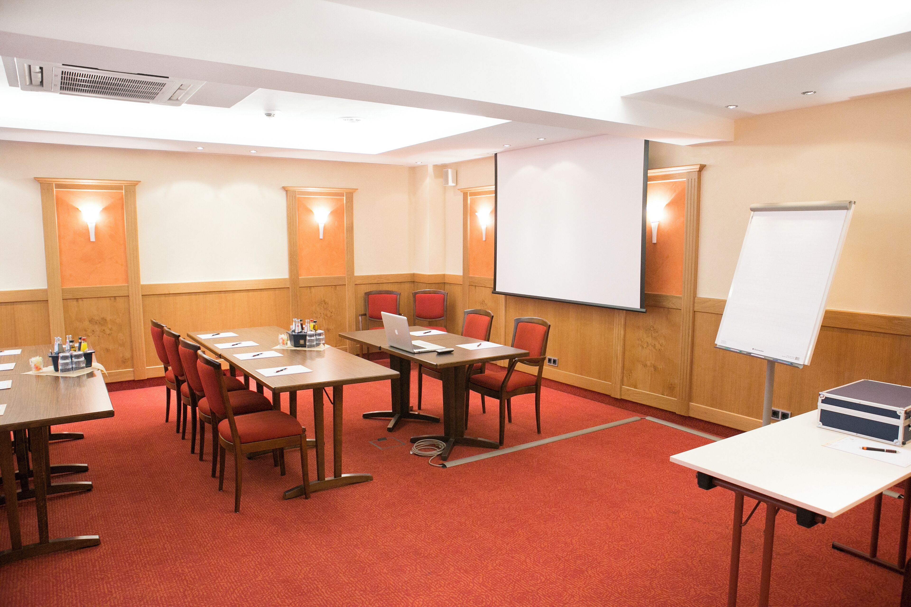Un salón de conferencias con una larga mesa, varias sillas, una pizarra y una pantalla de proyector.