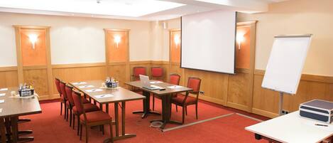 Un salón de conferencias con una larga mesa, varias sillas, una pizarra y una pantalla de proyector.