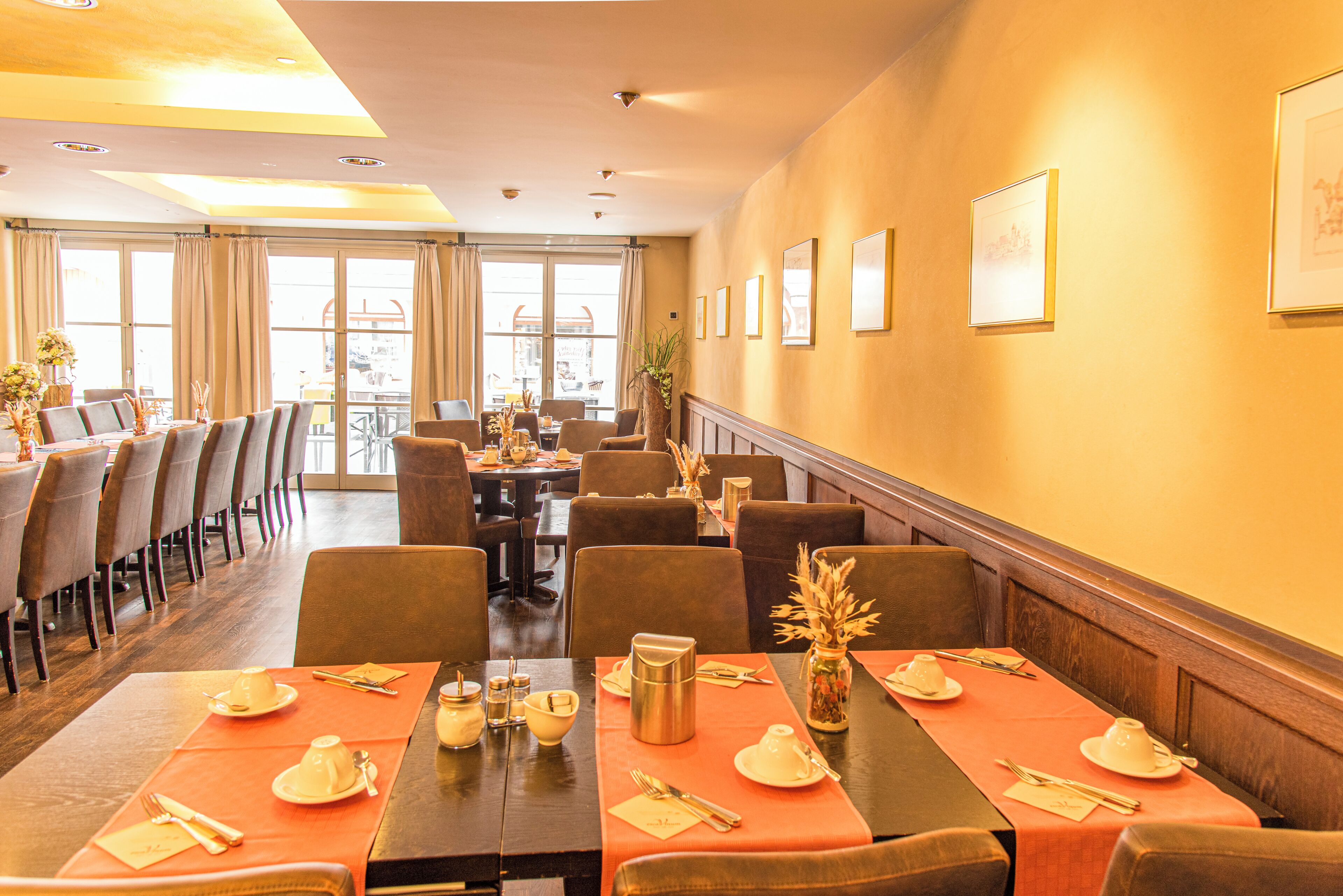 A dining area with tables set for service, chairs arranged around them, and a view through large windows.