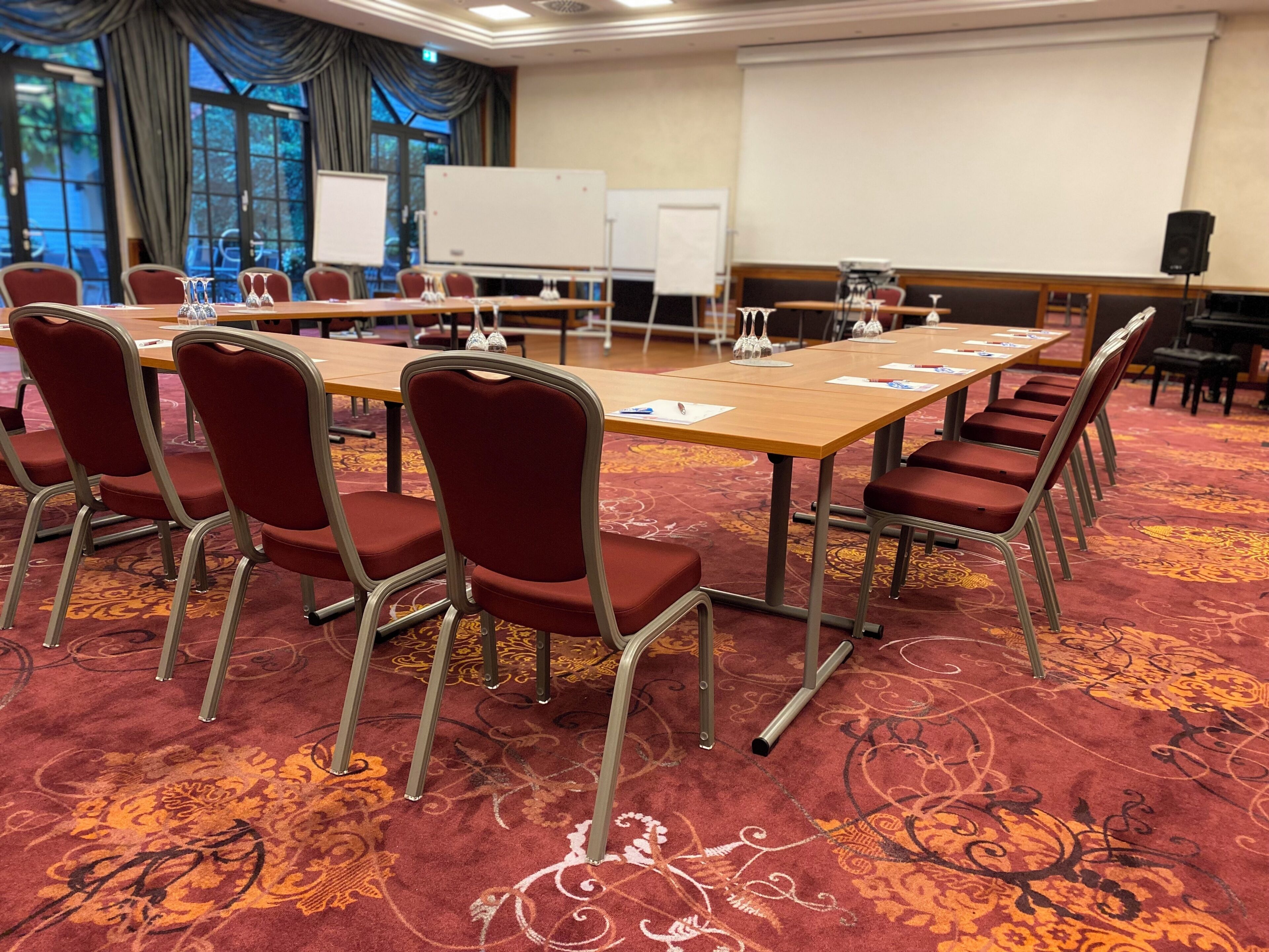 Un salón de conferencias con una larga mesa, sillas rojas, una pantalla de proyector y una pizarra.