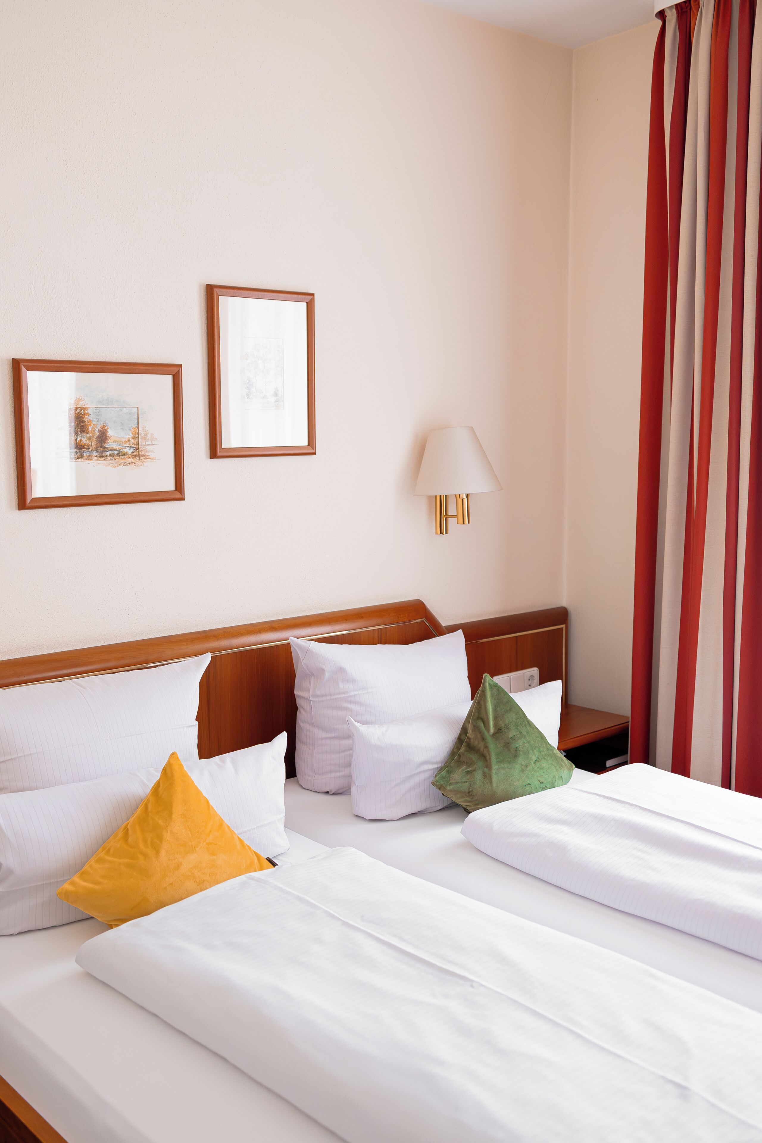 A hotel room with a bed, pillows, a nightstand, a lamp, and two framed pictures on the wall.