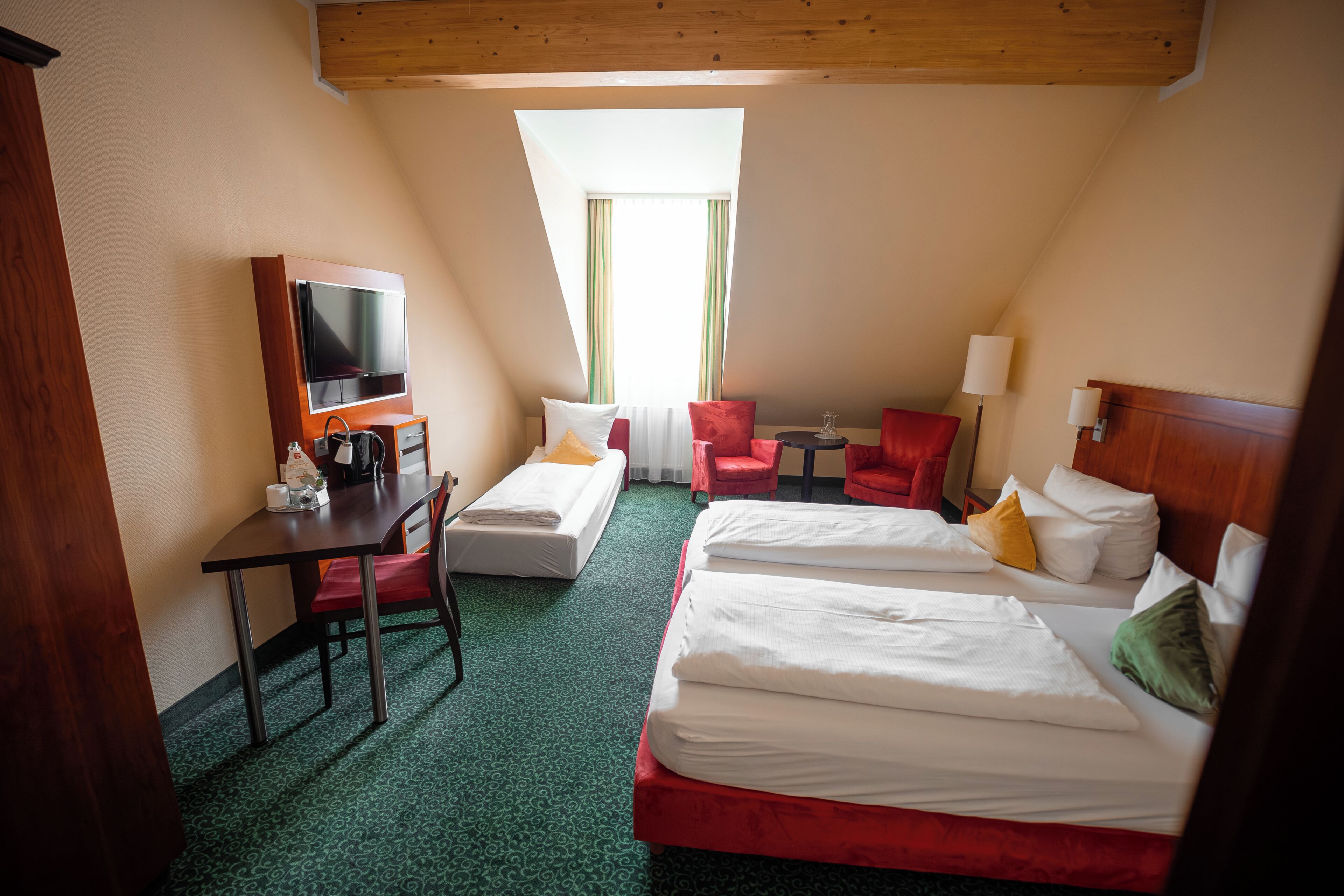 A hotel room with two beds, a desk with a chair, a TV, and a small table.