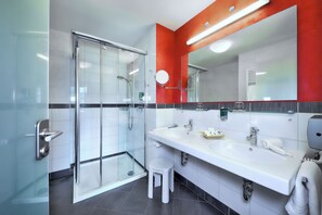 Ein modernes Badezimmer mit Duschkabine aus Glas, einem weißen Waschtisch mit großem Spiegel und einem Handtuchhalter.
