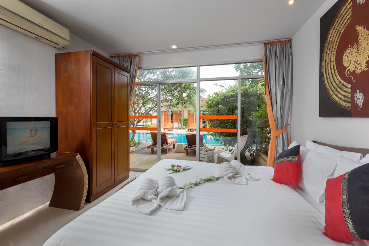 A hotel room with a bed, a TV, a wooden wardrobe, and a balcony with a pool view.