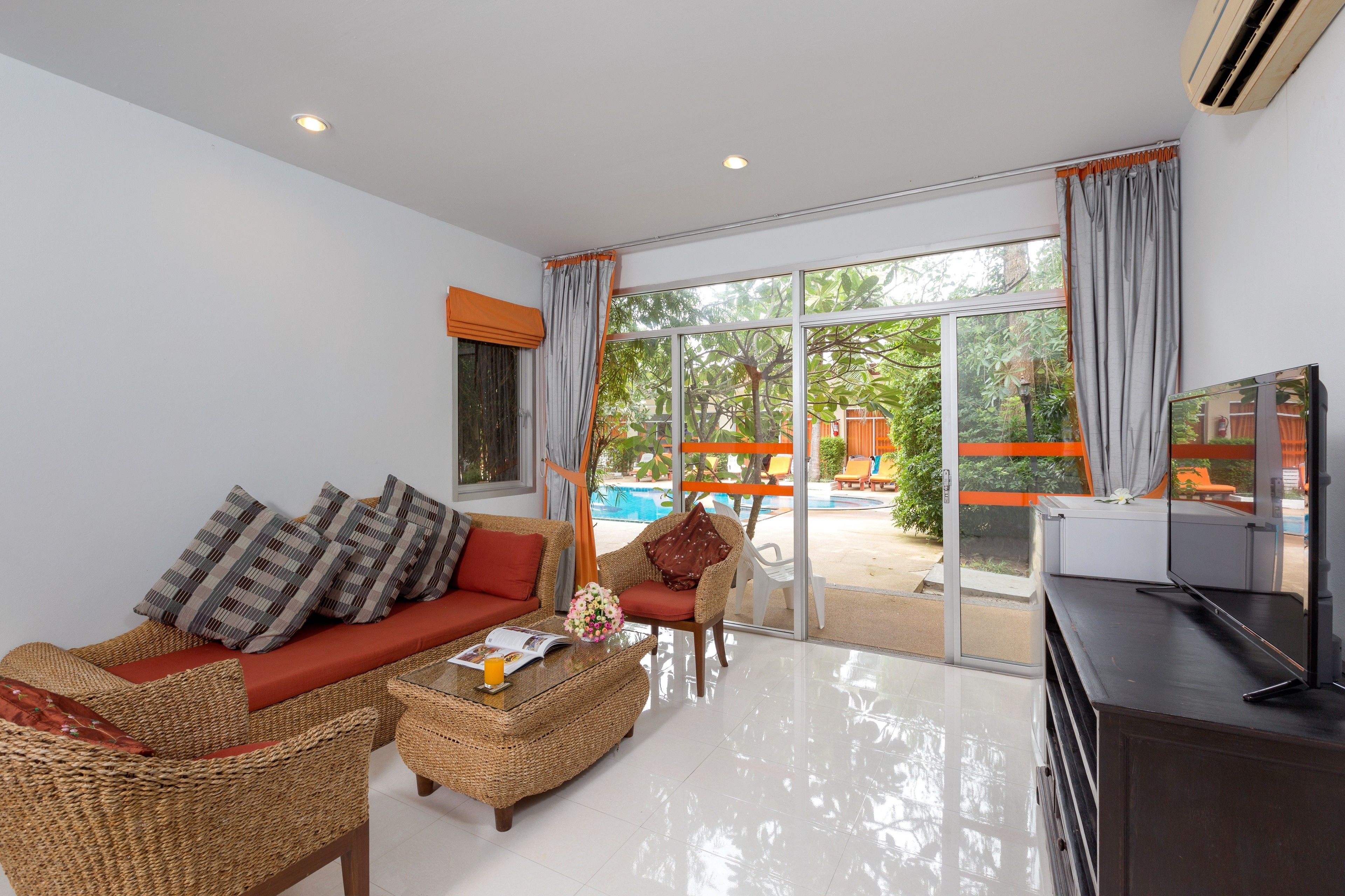 A modern living room with a sofa, armchairs, a coffee table, and a TV. Large windows offer a view of a pool and outdoor furniture.