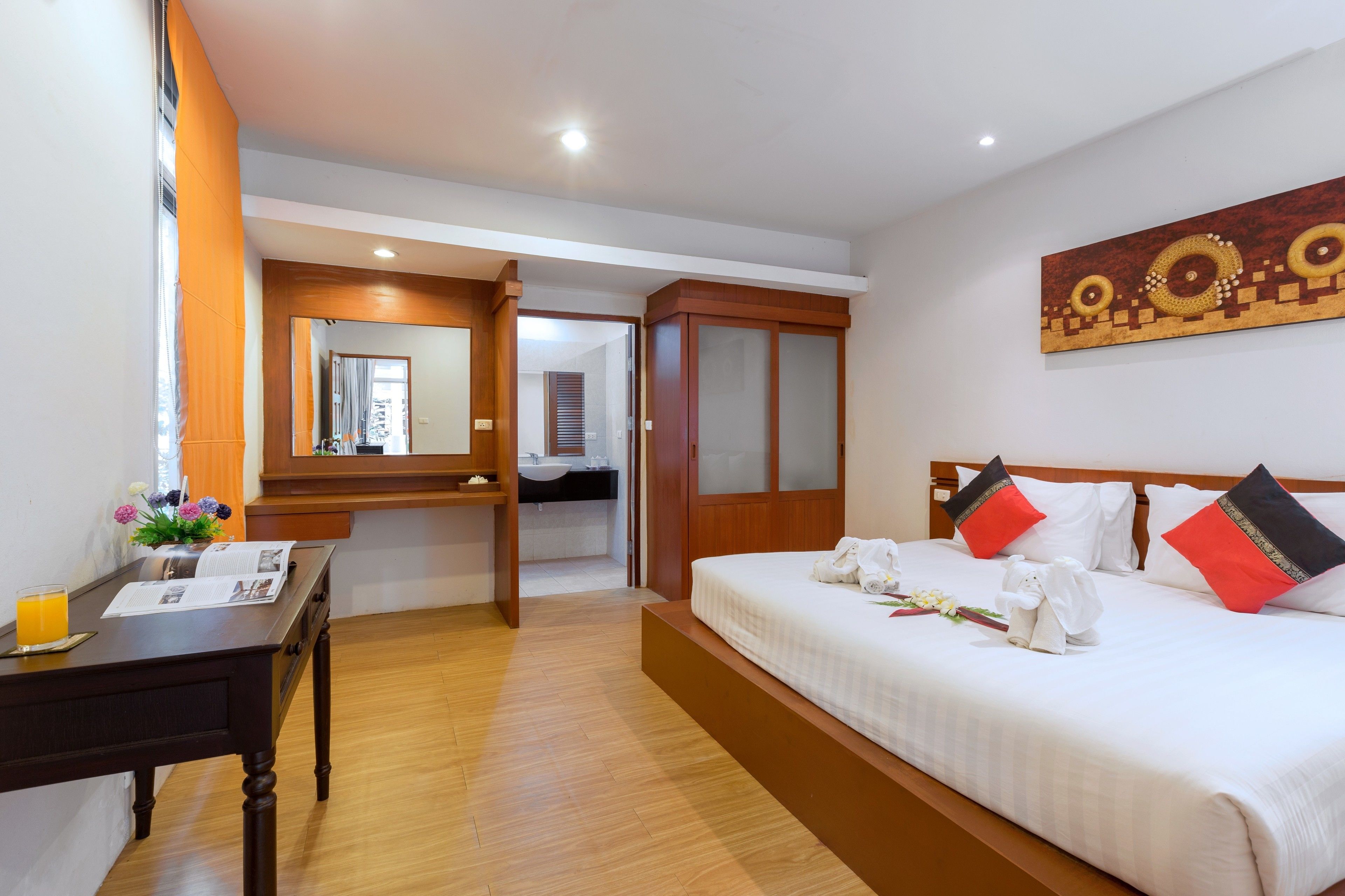 Habitación de hotel con cama, escritorio, espejo y baño visible a través de una puerta abierta.