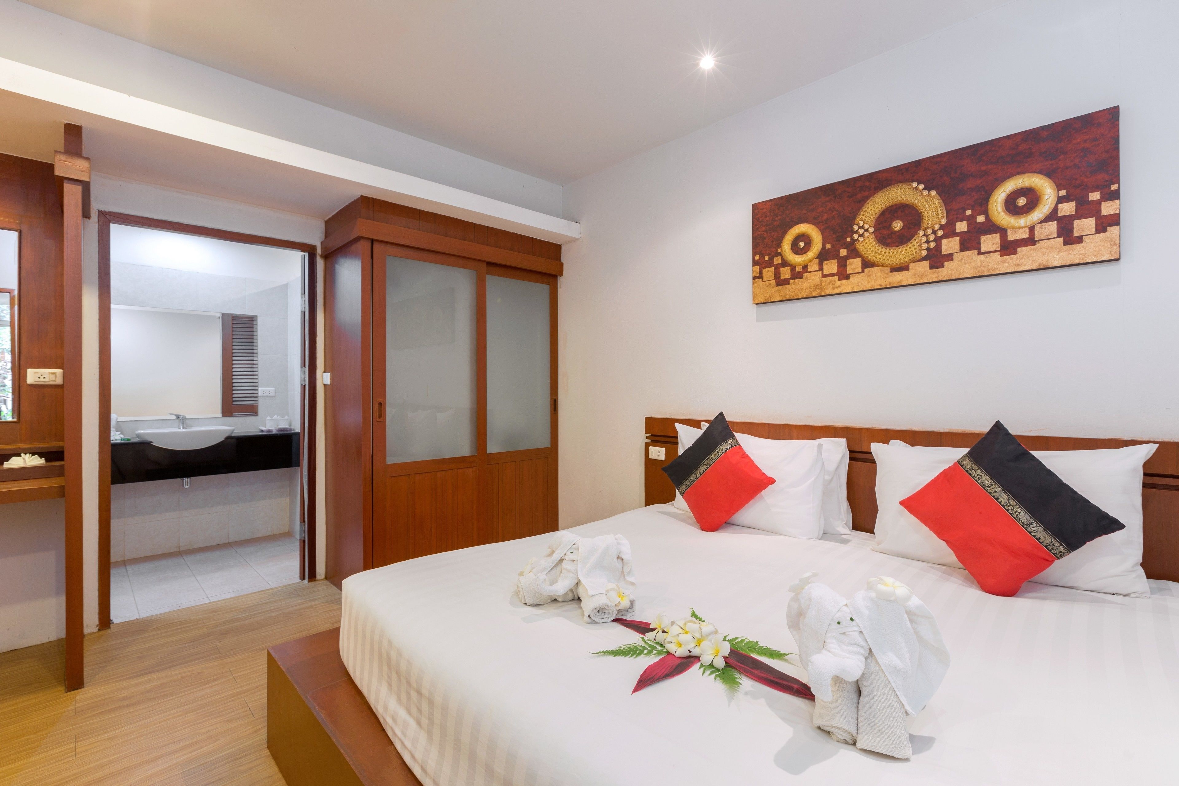 Une chambre d’hôtel avec un lit, une armoire en bois, une salle de bain avec un lavabo et un tableau au mur.