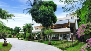 A modern building with a curved driveway, surrounded by lush greenery and palm trees. - Phuket Sea Resort (Rawai)