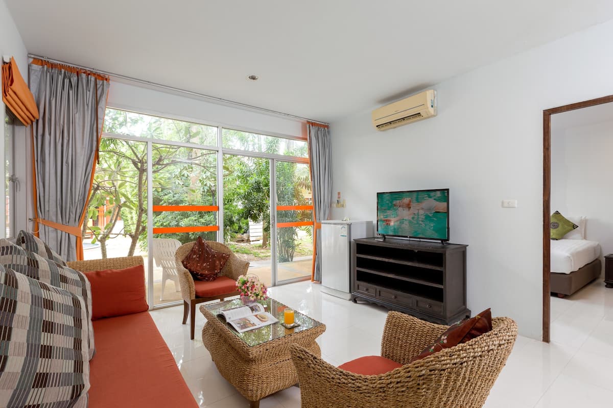 A modern living room with a sofa, a coffee table, wicker chairs, a television, and a refrigerator.
