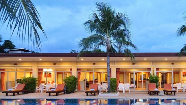 A hotel with a swimming pool, palm trees, and lounge chairs. - Phuket Sea Resort (Rawai)