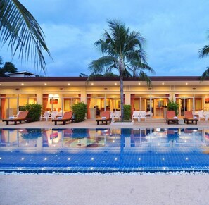 Un hotel con piscina, palmeras y sillones de descanso.