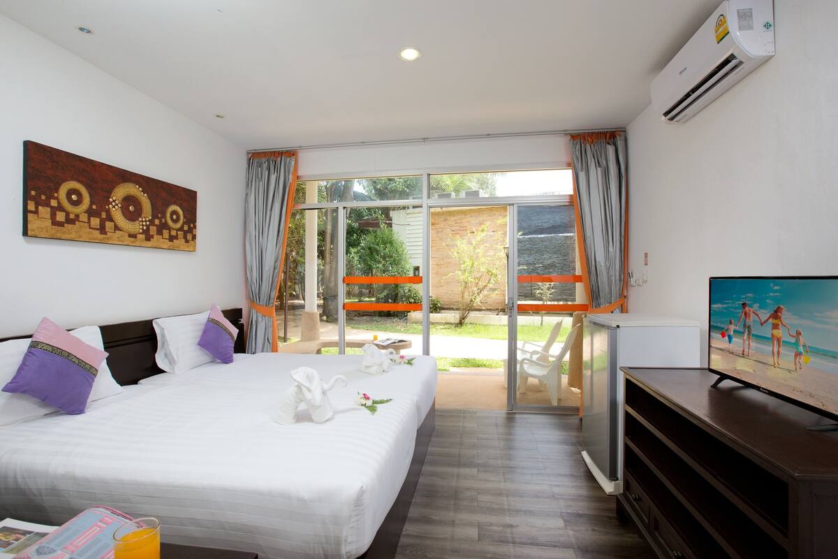 A hotel room with a bed, a television, and a sliding glass door leading to an outdoor area.