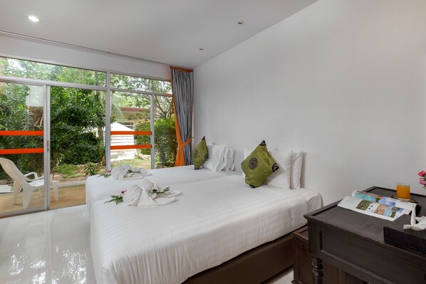 Habitación de hotel con dos camas, un ventanal grande y vistas al exterior con vegetación.
