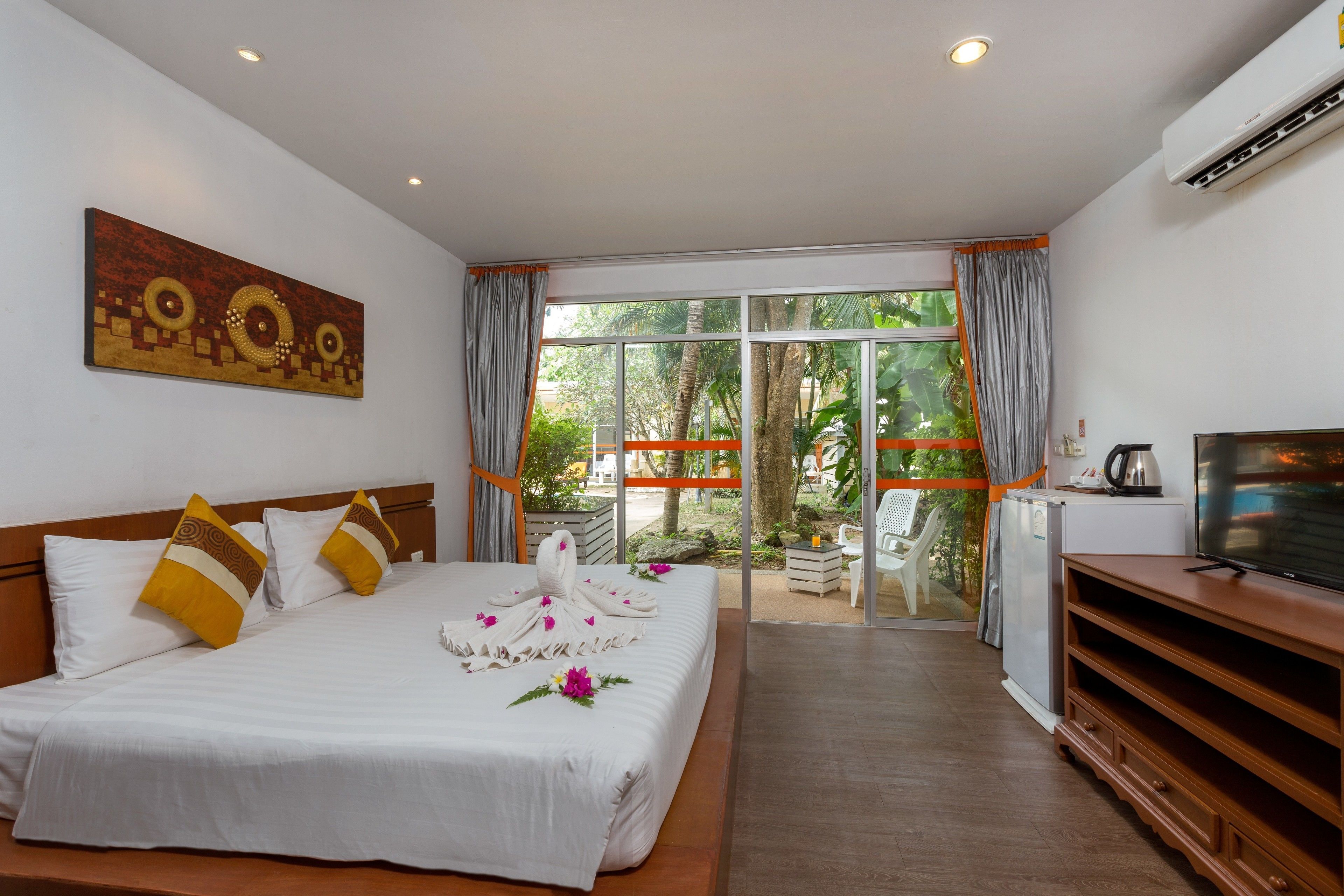 A hotel room with a bed, a TV, and a view of greenery outside.